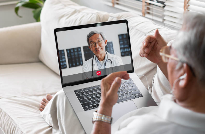 Elderly employee looking at laptop screen conversing with a telehealth doctor